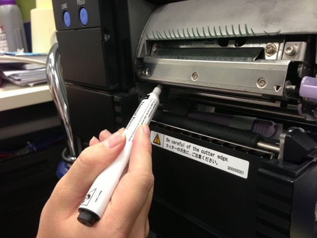 A cleaning pen being used on a Sato thermal printer