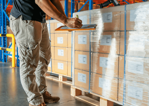 A worker checking on stretch-wrapped pallets inside a warehouse