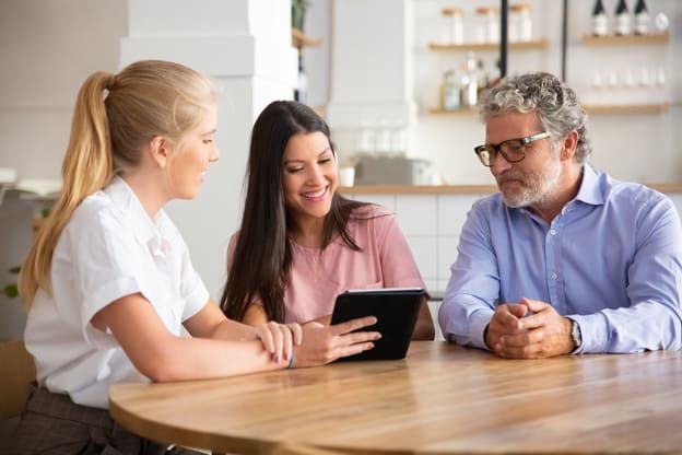 female-agent-manager-meeting-with-couple-young-mature-customers-presenting-content-tablet